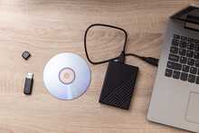 Digital Custodians Of Information. External Hard Drive, Cd And Usb Flash Drive, Laptop On A Wooden Table