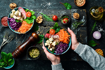 Female hands holding a bowl of vegan lunch: tofu cheese, spinach, cabbage, radishes and carrots. The concept of healthy eating. Top view.