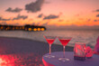 Two cocktail drinks with blur beach and colorful sunset sky in the background. Luxury outdoor leisure lifestyle, relaxing and romantic colors on a summer evening. Luxury romance with outdoor drinks