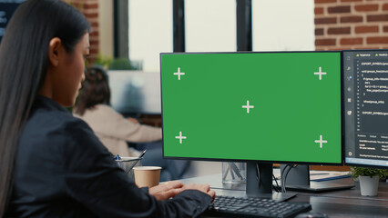 Focus on computer screen with green screen chroma key mockup in front of asian programer writing code in software development agency. Database coder programming sitting at desk.