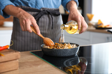 Young man pouring oil into frying pan with rice in kitchen, closeup