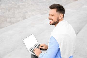 Wall Mural - Handsome businessman working with laptop on stairs outdoors