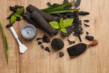 Wall Mural - Flatlay of bamboo activated charcoal and charcoal mask and scrub decorate in wooden dish with green leaf in wooden background 