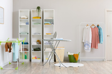 Poster - Interior of modern laundry room with ironing board and shelf units with different clothes