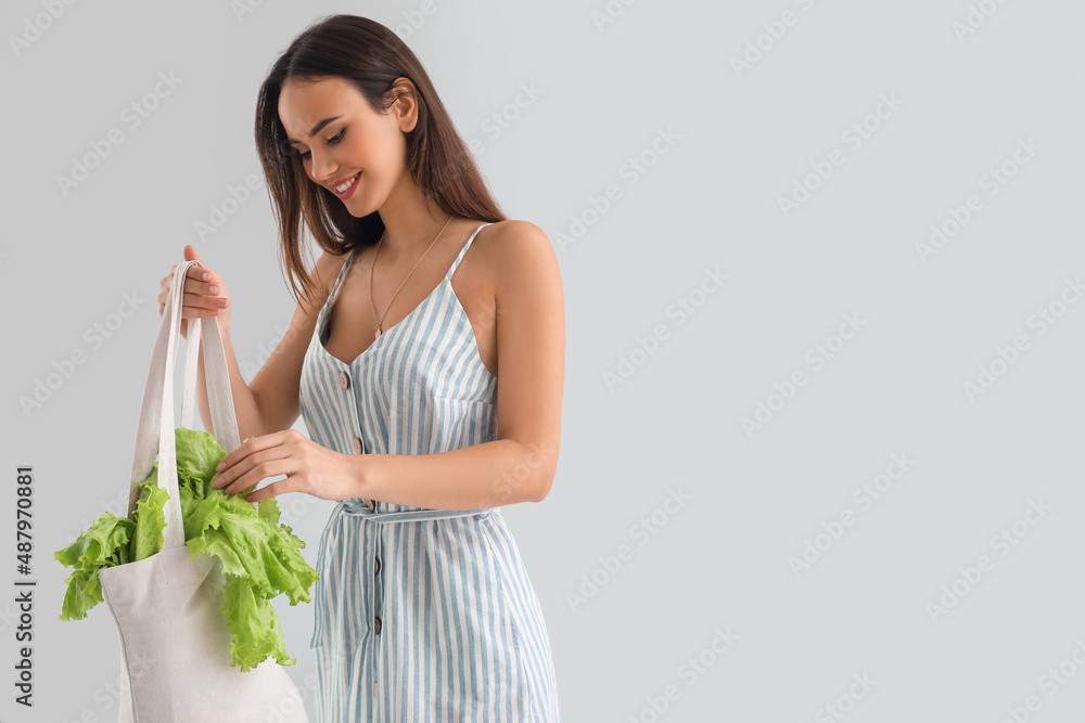 Young woman with shopping bag and lettuce on light background