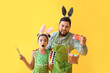 © Pixel-Shot - Little girl, her father with Easter eggs, paints and brushes on yellow background