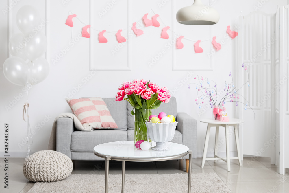 Vase with tulips and Easter eggs on table in living room interior
