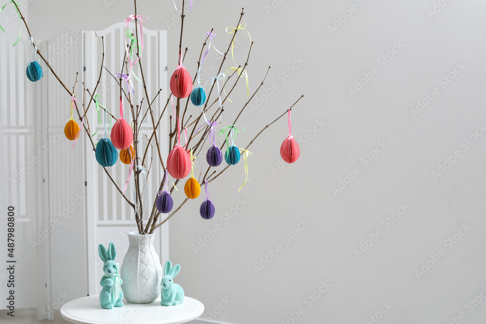 Tree branches with Easter decor in vase and rabbits on table in light room