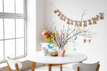 Dishware And Tree Branches Decorated With Easter Eggs On Dining Table In Light Room