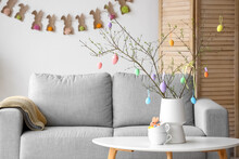 Tree Branches Decorated With Easter Eggs In Vase On Table Near Sofa