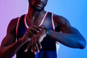 Wall Mural - Cropped view of young black sportsman checking his smartwatch in neon light, closeup