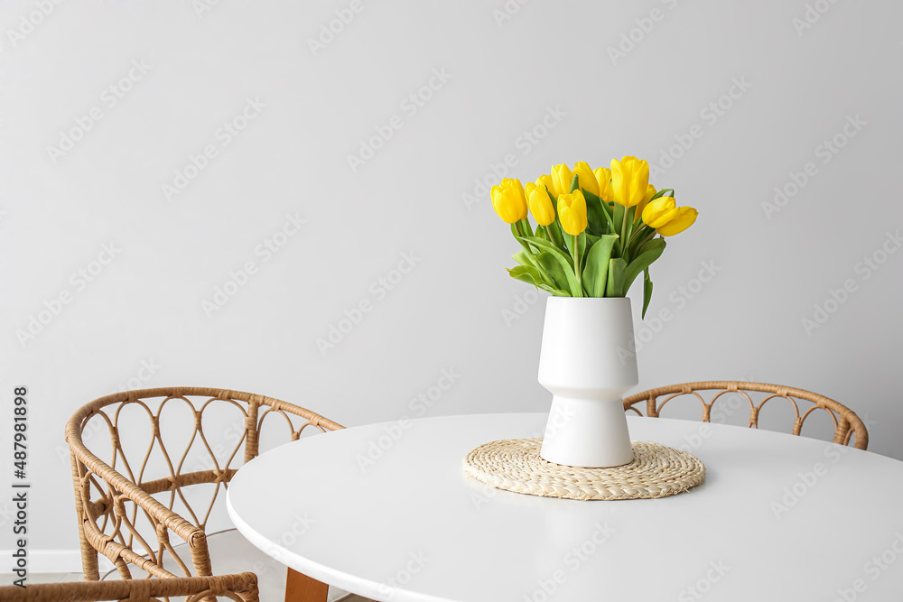 Vase with beautiful tulips on dining table near light wall