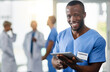 © Delmaine D/peopleimages.com - Staying current is an important part of my job. Portrait of a young doctor using a digital tablet with his colleagues in the background.