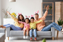 Little Children With Easter Rabbits And Their Parents Sitting On Sofa At Home
