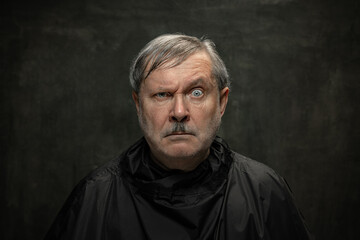 Portrait of angry senior man looking at camera isolated on dark vintage background. Concept of emotions, fashion, beauty, self-reinvention