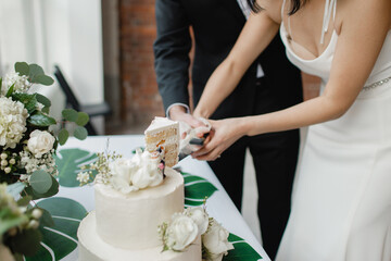 Wall Mural - The gorgeous bride and groom cut a small modern wedding cake on a table with various decorations Newlyweds cutting the wedding cake Young happy couple cut white cake at the end of a wedding day 