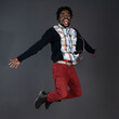 © Svyatoslav Lypynskyy - Emotionally motivated, positive, carefree african american young man in red jeans and black sweater happy jumping in studio isolated on dark grey background