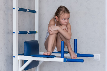 little girl sits on an exercise machine for sports with a sad pensive face