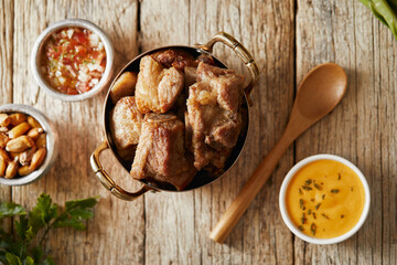 Homemade fritada a typical ecuadorian dish that consists on braised pork. It’s served on a white plate with chilli and tostado, with a traditional and wooden background 