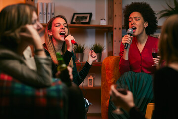 Happy multiracial friends are sitting at home and having fun on karaoke night.