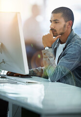 He always gives his work one hundred percent focus. Shot of a young designer deep in thought while working on a computer in a modern office.