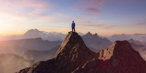 Wall Mural - adventurous man hiker standing on top of a rocky mountain overlooking the dramatic landscape at suns