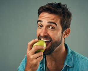 Poster - Snacking the healthy way. Studio portrait of a handsome young man eating an apple against a grey background.