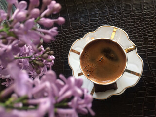 Poster - A top view of a cup of a coffee on a leather table and purple flower