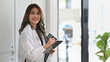 Beautiful female doctor in white coat with stethoscope holding her patient chart and smiling to camera.