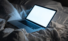 a laptop putting on the bed in the dark with screen on 