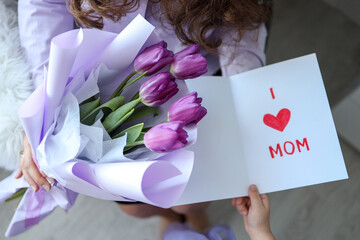 Happy mother's day! The child's daughter congratulates her mother and gives her flowers tulips and a postcard: I love you, mom