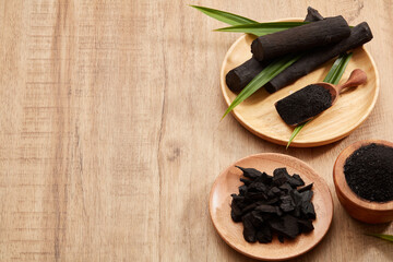 Wall Mural - Flatlay of bamboo activated charcoal and charcoal powder decorated with green leaf in wooden background 