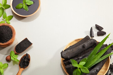 Wall Mural - Flatlay of bamboo activated charcoal and charcoal mask and scrub decorate 
 with green leaf in white background 