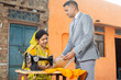 © GAJENDRRA BHATI  - Bank person or financial advisor showing document to indian woman while she is working on sewing cloths on sewing machine. Small Business or startup loan concept.