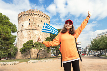 Happy student girl with a Greek flag on the background of a White Tower in Thessaloniki. The concept of citizenship or learning Greek language in university