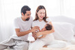 © Rakchanok - Selective focus of Asian man and woman holding newborn baby in bed at home. Happy family smiling with adorable infant, young parents holding little sweet toddler baby, mom hold toddler with love.