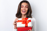 Fototapeta Na ścianę - Young woman in a cocktail dress, gold chain, bright spring pink makeup on a white background. Holds a gift box for March 8 and smiles cheerfully.