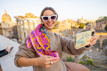 Wall Mural - Woman takes selfie photo on background of the Roman Forum, ruins at the center of Rome on a sunset. Concept of traveling famous landmarks in Italy