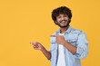 © insta_photos - Happy excited young indian man looking at camera pointing aside with fingers hand gesture at copy space advertising new promotion, presenting sale offer standing isolated on yellow background.