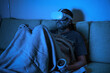 © scaliger - Man sitting on sofa uses virtual reality headset at night