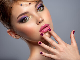 Portrait of a beautiful woman with bright makeup. Closeup female face with purple eye make-up. Pretty, sexy girl with violet nails near face. Stylish fashion model with a short slick hair