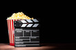 Cinema concept. Popcorn in a box and movie clapper on wooden table under beam of light against black background