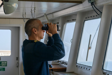 Wall Mural - Deck officer with binoculars on navigational bridge. Seaman on board of vessel. Commercial shipping. Passenger ship.