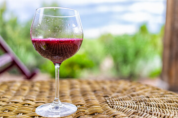 Glass of dark red purple wine or cranberry juice on wicker table in Santa Fe desert garden backyard with closeup of one drink and bokeh background of scenery