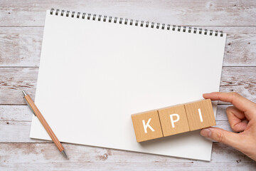 KPIのイメージ｜「KPI」と書かれた積み木、ペン、ノート、人の手