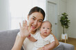 © Nattakorn - Point of view, Young Asian mother and her newborn baby smiling and say hello / goodbye via video call or facetime feeling happy