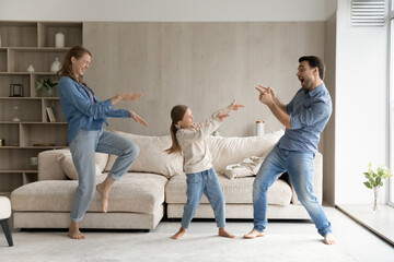 Wall Mural - Excited funny parents and sweet happy daughter kid playing western, making gun hand gunshots, dancing to hip hop music in living room, laughing, having fun, enjoying active games together