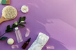 SPA beauty treatment with hygiene accessories, natural soap, essence oil, massage brush, bath bomb, sponges on purple background