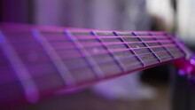 Acoustic Guitar Strings And Fretboard On Blurred Background. Musical Instrument For Performing Illuminated By Purple Neon Light In Room Extreme Closeup