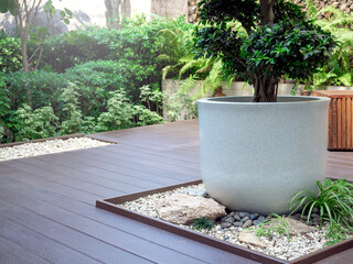 The big white terrazzo plant pot with a green tree on little stone garden space decoration on wood terrace near the green garden.